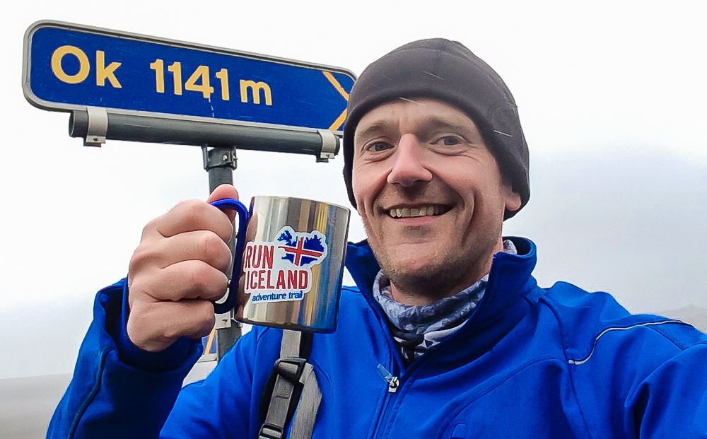 Peter Hobley holding mug in front of road sign that says Ok